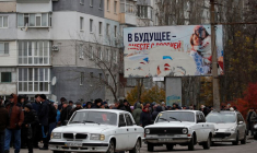 Des personnes attendent la distribution d'aide humanitaire, avec un panneau publicitaire pro-russe en arrière-plan, à Kherson