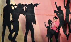 Une femme passe devant une fresque murale représentant des hommes armés visant des manifestants, allusion à la répression policière, dans une avenue de Tegucigalpa, le 27 novembre 2025 ( AFP / Orlando SIERRA )