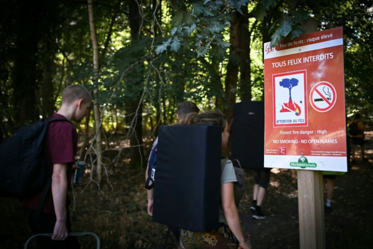 Des randonneurs passent devant devant un panneau "Tous feux interdits" au premier jour de la réouverture au public de la forêt de Fontainebleau partiellement dévastée par les flammes en juillet, le 22 août 2026 près d'Avon, en Seine-et-Marne  ( AFP / Lou BENOIST )