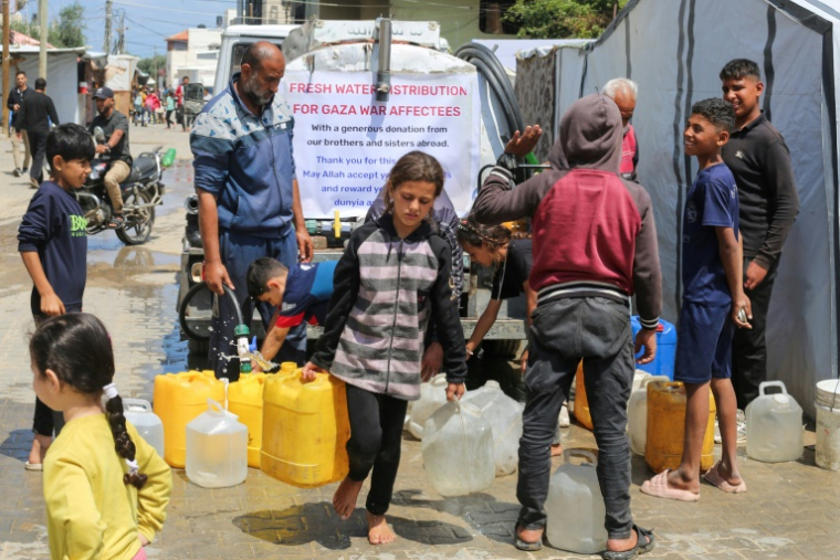 Des enfants palestiniens remplissent des bidons d'eau à un point de distribution au camp de réfugiés de Nousseirat, dans le centre de la bande de Gaza, le 5 mai 2025 ( AFP / Eyad BABA )