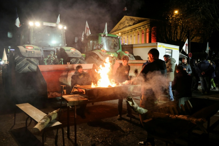 Des agriculteurs autour d'un barbecue près de leurs tracteurs garés devant l'Assemblée nationale, le 13 janvier 2026 à Paris ( AFP / Ludovic MARIN )