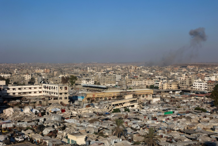 Une photo montre une vue d'un camp de déplacés installé sur ce qui était autrefois un terrain de football, avec en arrière-plan de la fumée qui s'élève pendant des rauds israéliens sur Gaza-ville, le 4 septembre 2025 ( AFP / Omar AL-QATTAA )