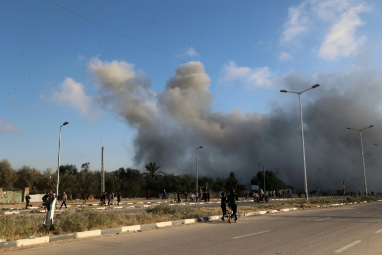 De la fumée lors d'une frappe israélienne alors que des Palestiniens marchent sur une route utilisée pour atteindre un point de distribution d'aide de la Fondation humanitaire de Gaza (GHF,) près du camp de réfugiés de Nousseirat, dans le centre de la bande de Gaza, le 25 juin 2025 ( AFP / Eyad BABA )