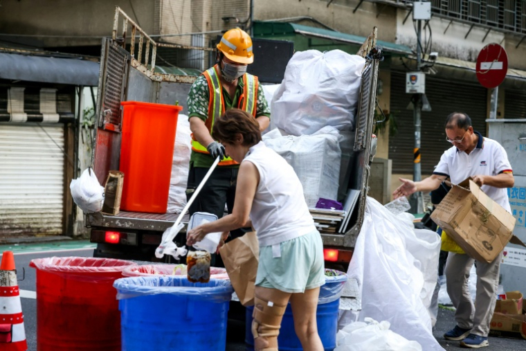 Une habitante (c) jette des déchets alimentaires dans un seau, tandis qu'un autre résident (d) dépose son plastique à côté d'un camion de collecte, à Taipei, le 19 juin 2025 ( AFP / I-Hwa Cheng )