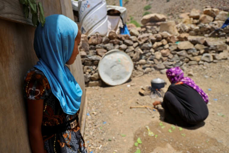 Une petit-fille (G) de Saeedah Mohammed, déplacée avec sa famille dans le camp d'Al-Manij, près de Taëz, dans le sud-ouest du Yémen, la regarde préparer à manger devant leur abri de fortune, le 21 mai 2026 ( AFP / Ahmed al-Basha )