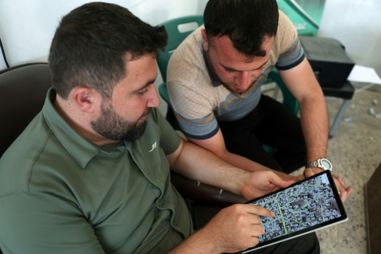 L'architecte syrien Abdel Aziz al-Mohammed (à gauche) montre sur une tablette une carte qu'il a créée, révélant l'état détaillé de chaque maison de son village de Tal Mardikh, dans la province d'Idlib, au nord-ouest de la Syrie, le 2 juin 2025 ( AFP / OMAR HAJ KADOUR )