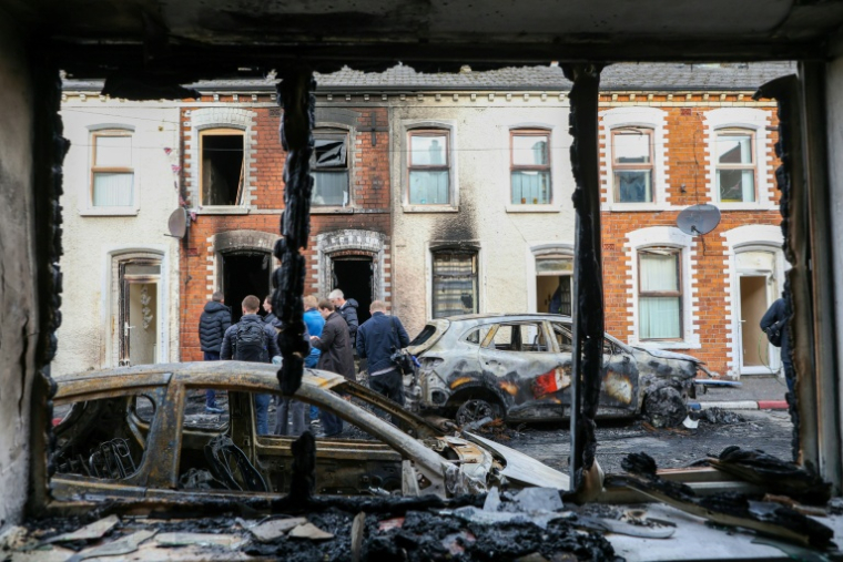 Des habitants observent des voitures et de smaisons incendiées au lendemain de manifestations qui ont dégénéré en violences, dans l'est de Belfast, en Irlande du Nord, le 10 juin 2026 ( AFP / Paul Faith )