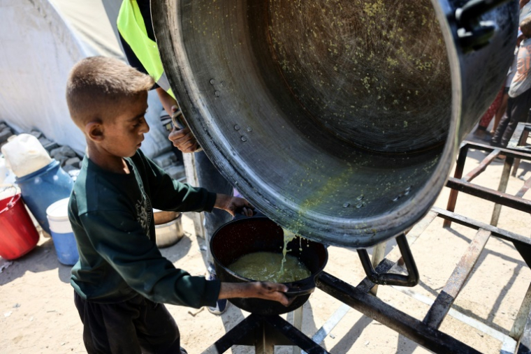 Un garçon palestinien reçoit les dernières gouttes d'une soupe aux lentilles à un point de distribution de nourriture dans la ville de Gaza, le 1er août 2025 ( AFP / Omar AL-QATTAA )
