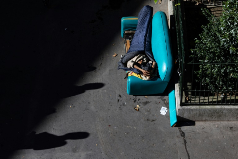 Un réfugié afghan dort sur un canapé installé Place de la Chapelle à Paris le 5 octobre 2024 ( AFP / JOEL SAGET )