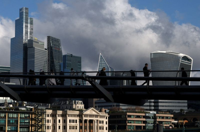 Des personnes marchent près du Millenium Bridge avec le quartier financier de la City de Londres derrière