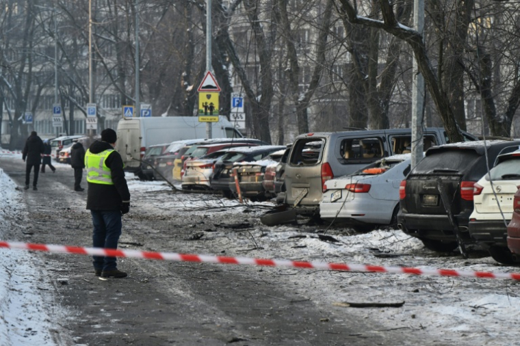 Des habitants devant des voitures endommagées sur un site où des débris de drones russes sont tombés durant une attaque arérienne massive russe, à Kiev en Ukraine le 20 janvier 2026 ( AFP / Genya SAVILOV )