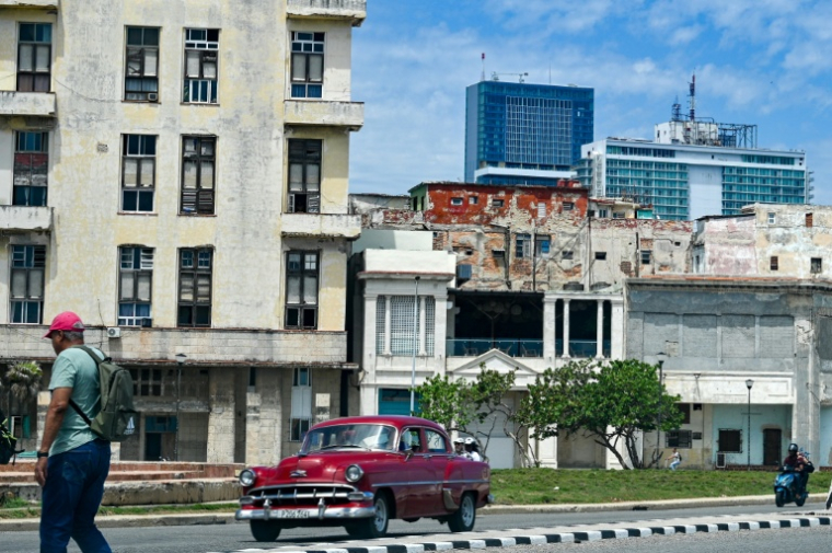 Un homme marche dans la rue tandis qu'une voiture classique passe, avec en arrière-plan l'hôtel Iberostar Selection et l'hôtel Habana Libre Melia, à La Havane, le 2 juin 2026 ( AFP / ADALBERTO ROQUE )