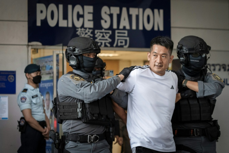 She Zhijiang, fondateur chinois du groupe Yatai, qui aurait construit un centre d'arnaque à la frontière entre la Thaïlande et la Birmanie, est escorté par des policiers thaïlandais le 12 novembre 2025 à Bangkok ( AFP / Chanakarn Laosarakham )