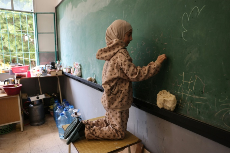 Une jeune fille effectue des calculs arithmétiques sur un tableau dans une salle de classe d'une école publique transformée en refuge pour personnes déplacées à Dekwaneh, au nord de Beyrouth, le 24 mars 2026 au Liban ( AFP / Anwar AMRO )