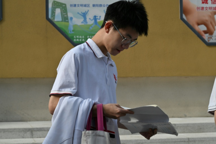 Un lycéen consulte un manuel avant d'affronter l'examen national d'entrée à l'université, connu sous le nom de "Gaokao", à l'extérieur d'un lycée de Pékin, le 7 juin 2025 ( AFP / Adek BERRY )