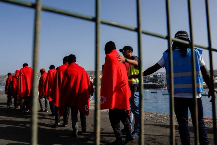 La police Frontex accompagne plusieurs migrants vers une tente de la Croix-Rouge après leur débarquement d'un navire des garde-côtes espagnols, dans le port d'Arguineguin