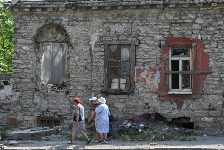 Des femmes passent devant une maison détruit par les combats, dans la ville ukrainienne de Marioupol contrôlée par la Russie, le 16 juillet 2025 ( AFP / Olga MALTSEVA )