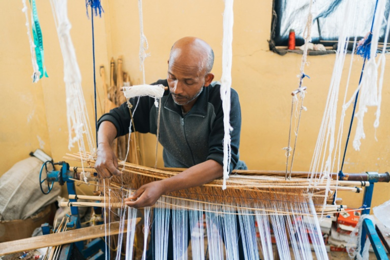 Le tisserand Gety Derza travaille sur un métier à tisser traditionnel en bois dans un atelier du quartier Shiromeda à Addis Abeba, le 7 octobre 2025 en Ethiopie ( AFP / Sehin Tewabe )