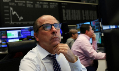 Un courtier en bourse regarde ses écrans devant le graphique de l'indice des prix des actions DAX à la bourse de Francfort