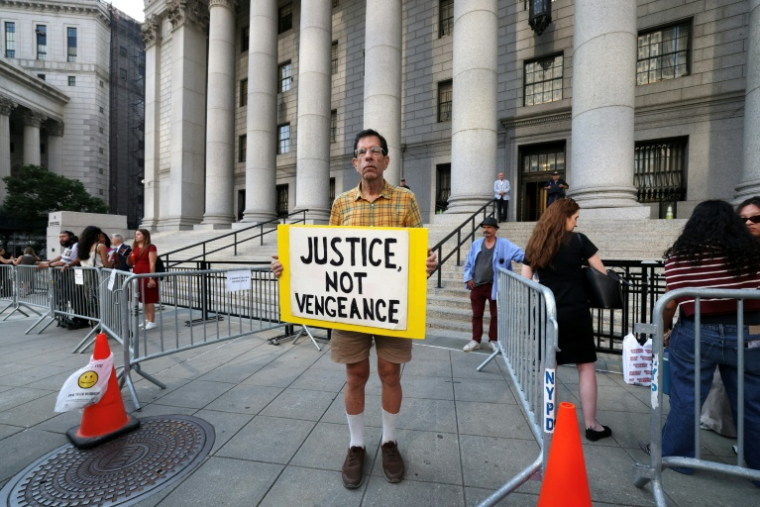 Un soutien de Luigi Mangione avec une pancarte disant "Justice, pas vengeance" devant le tribunal fédéral de Manhattan, à New York, devant lequel comparaissait Luigi Mangione le 14 août 2026  ( AFP / TIMOTHY A. CLARY )