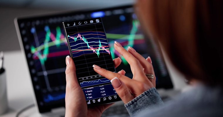 jeune adulte tenant un écran avec des graphiques de cours de Bourse (Crédits: Adobe Stock)