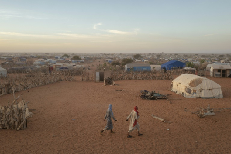Deux hommes passent devant des abris et des tentes dans le camp de réfugiés de M'berra, dans le sud-est de la Mauritanie, qui accueille 120 000 réfugiés fuyant la violence et l'instabilité au Mali, à Bassikonou, le 3 novembre 2025. ( AFP / MICHELE CATTANI )