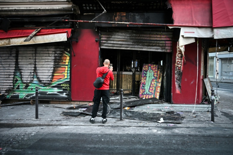 Un passant en prend photo la façade du restaurant "La Barrique" incendié et vandalisé près de la place de la République, au lendemain d'une manifestation contre la vie chère, le 18 octobre 2026 à Paris ( AFP / Matthieu RONDEL )