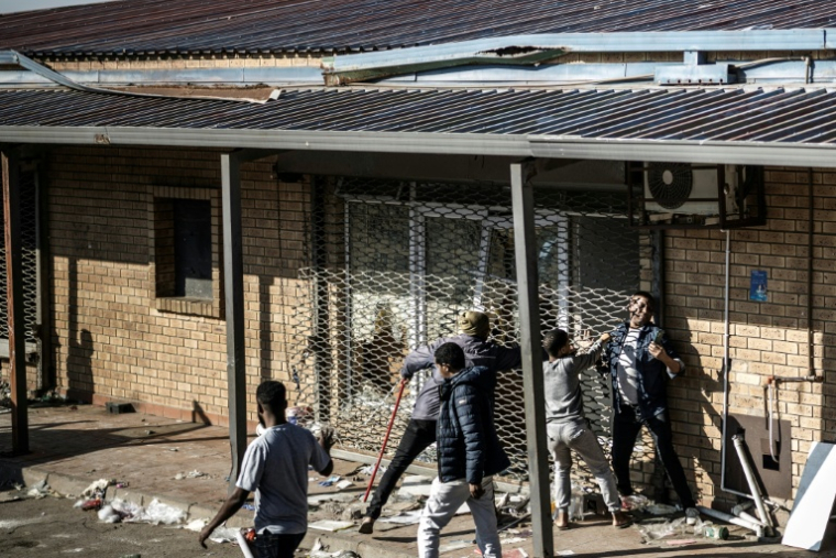 Un homme tente de se faufiler sous le rideau métallique d'un magasin pillé dans la nuit, le 1er juillet 2026 à Durban, en Afrique du Sud ( AFP / MARCO LONGARI )