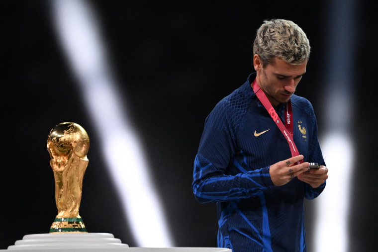 Le joueur Antoine Griezmann regarde sa médaille d'argent en passant devant le trophée de la Coupe du monde à Doha, au Qatar, le 18 décembre. ( AFP / KIRILL KUDRYAVTSEV )