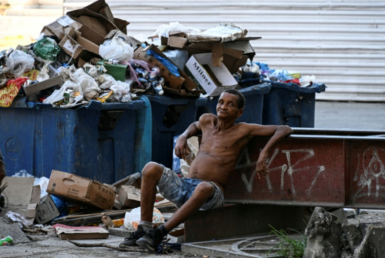 Un sans-abri assis devant des conteneurs à ordures dans une rue de La Havane, le 21 juillet 2025 à Cuba ( AFP / Yamil LAGE )