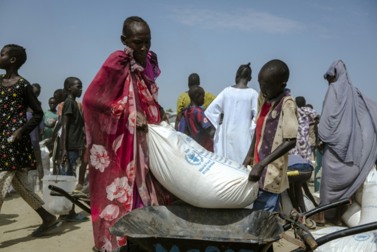 Un garçon et sa mère soulèvent un sac de maïs pour le charger dans leur brouette, dans un centre de distribution du camp de déplacés à Bentiu, dans l'État d'Unity, au Soudan du Sud, le 6 novembre 2025 ( AFP / Rian COPE )