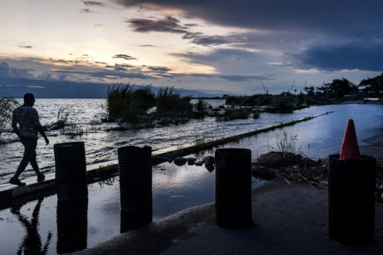 Un homme marche sur une étroite bande médiane encore accessible d'une route inondée le long du lac Tanganyika, le 8 mai 2025 à Bujumbura ( AFP / Luis TATO )