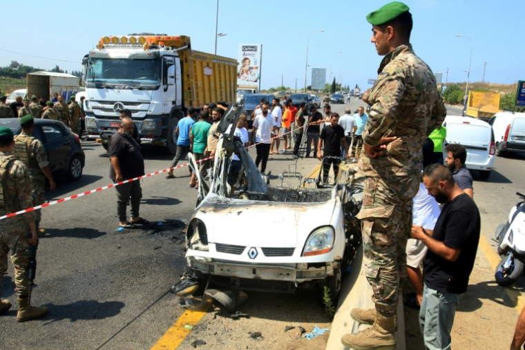 Des soldats de l'armée libanaise près de l'épave d'un véhicule,  cible d'une frappe israélienne, sur l'autoroute près du village d'Ansarieyh, au sud de la ville côtière de Sidon, le 8 août 2025 ( AFP / Mahmoud ZAYYAT )