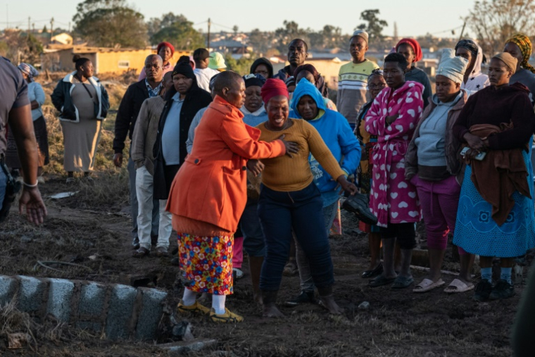 Des habitants et des familles en état de choc alors que des membres des services médicaux d'urgence (EMS) sortent des corps d'une maison après des inondations hivernales, le 12 juin 2025 près de Mthatha, en Afrique du Sud ( AFP / EMMANUEL CROSET )