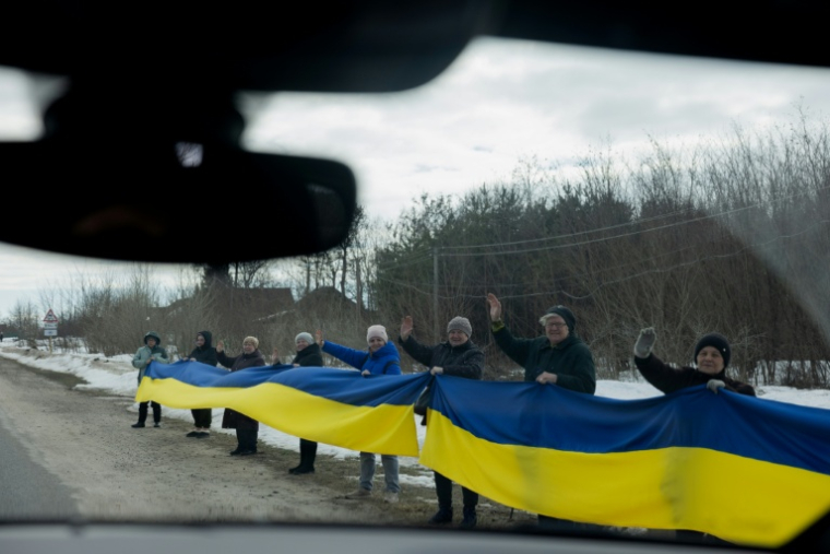 Des personnes tiennent un drapeau ukrainien le long d'une route pour accueillir un convoi de soldats libérés par les Russes après un échange de prisonniers, le 6 mars 2026 dans un lieu non précisé dans le nord de l'Ukraine ( AFP / Tetiana DZHAFAROVA )