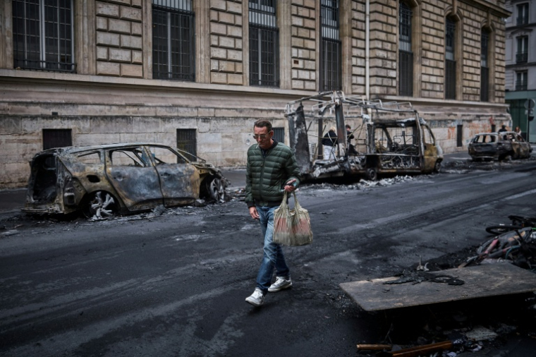 Un homme passe devant une rangée de véhicules calcinés, détruits lors d'une manifestation nationale contre la "vie chère" dans le centre de Paris, le 19 octobre 2026 ( AFP / Kiran RIDLEY )
