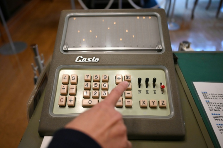 Un guide fait une démonstration sur une calculatrice Casio 14-A, le 25 novembre 2025 au musée Toshio Kashio à Tokyo ( AFP / GREG BAKER )