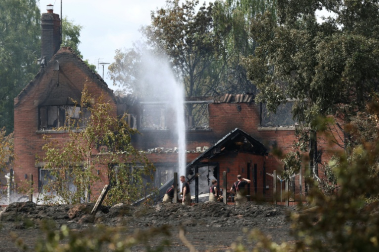 Des pompiers arrosent les ruines encore fumantes d'une maison endommagée par un incendie, au sud de Stourbridge, dans le centre de l'Angleterre, le 14 août 2026 ( AFP / Darren Staples )