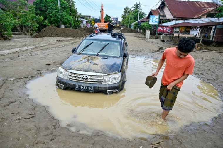 Un homme passe devant une voiture embourbée à la suite de crues soudaines à Meureudu, dans la province d’Aceh, en Indonésie, le 28 novembre 2025 ( AFP / CHAIDEER MAHYUDDIN )