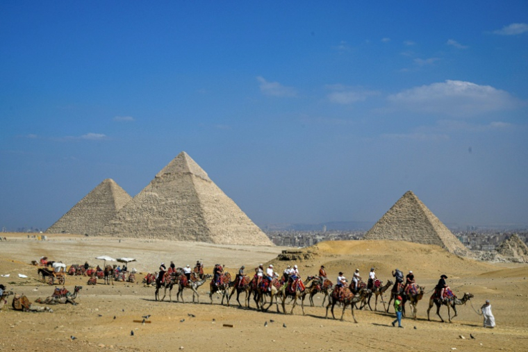 Des touristes à dos de chameau visitent la nécropole des pyramides de Gizeh, le 7 novembre 2025 en Egypte ( AFP / Khaled DESOUKI )