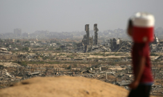 Un enfant palestinien portant un bidon d'eau passe devant des destructions sur une route côtière au nord-ouest du camp de Nousseirat, empruntée par des Palestiniens déplacés se rendant vers le sud de la bande de Gaza, le 4 octobre 2025 ( AFP / Eyad BABA )