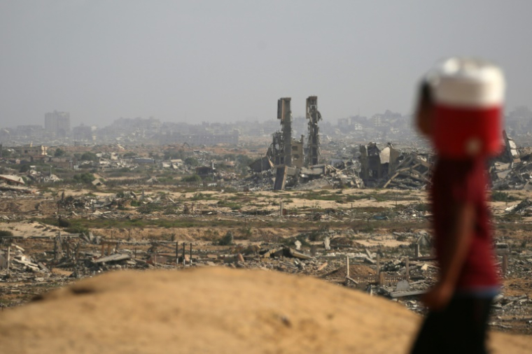 Un enfant palestinien portant un bidon d'eau passe devant des destructions sur une route côtière au nord-ouest du camp de Nousseirat, empruntée par des Palestiniens déplacés se rendant vers le sud de la bande de Gaza, le 4 octobre 2025 ( AFP / Eyad BABA )