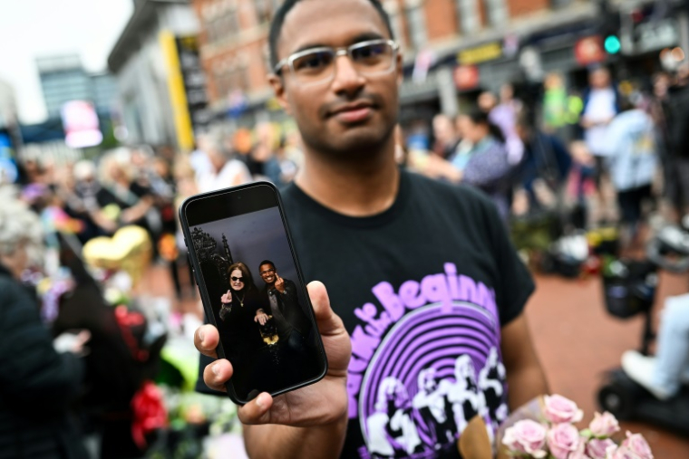 Un fan montre sur son téléphone portable une photo de lui et de l'auteur-compositeur-interprète britannique Ozzy Osbourne, devant mémorial improvisé sur le pont Black Sabbath, en hommage à l'artiste décédé, à Birmingham, dans le centre de l'Angleterre, le 23 juillet 2025 ( AFP / JUSTIN TALLIS )