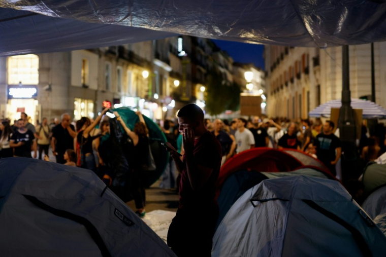 Un manifestant regarde son téléphone à côté de tentes dans le campement en établi en protestation contre les expulsions et la crise du logement sur la Puerta del Sol, à Madrid, le 27 septembre 2026 ( AFP / Oscar DEL POZO )