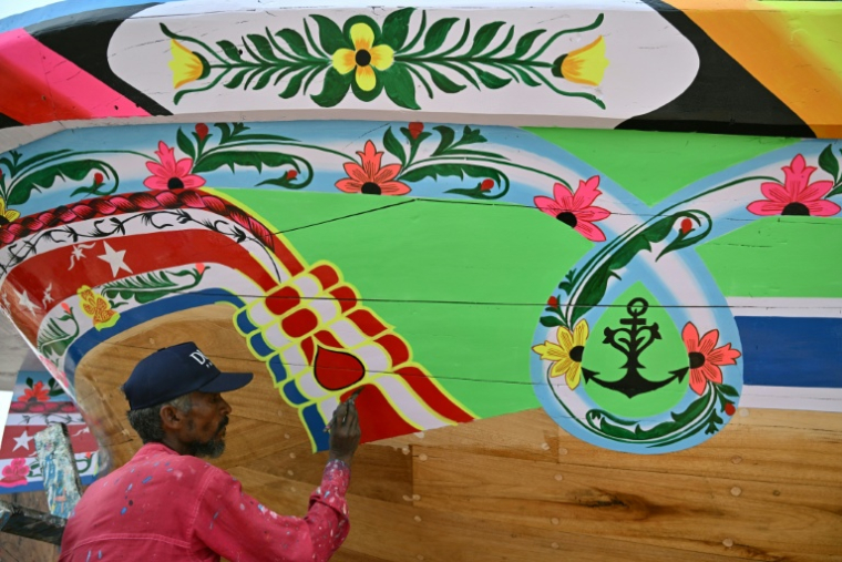L'artisan Muhammad Ismail peint des motifs sur un bateau traditionnel en bois, dans le quartier Ibrahim Hyderi à Karachi, Pakistan, le 8 juillet 2026 ( AFP / Asif HASSAN )