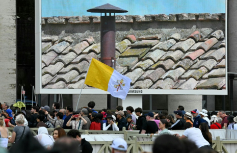 Des fidèles à Rome scrutent sur un écran la cheminée de la chapelle Sixtine au deuxième jour du conclave le 8 mai 2025 ( AFP / Andreas SOLARO )