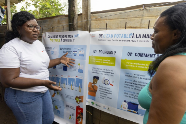 Une conseillère de la Croix-Rouge (G) explique à une habitante de Savane, un quartier de Matoury, en périphérie de Cayenne, comment traiter l'eau à domicile, le 6 juin 2026 ( AFP / Ronan LIÉTAR )