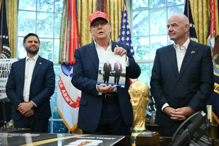 Le président américain Donald Trump, entouré du vice-président JD Vance et du chef de la FIFA Gianni Infantino, montre une photo sur laquelle il figure en compagnie de son homologue russe Vladimir Poutine, le 22 août 2025 à la Maison Blanche ( AFP / ANDREW CABALLERO-REYNOLDS )