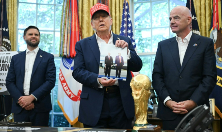 Le président américain Donald Trump, entouré du vice-président JD Vance et du chef de la FIFA Gianni Infantino, montre une photo sur laquelle il figure en compagnie de son homologue russe Vladimir Poutine, le 22 août 2025 à la Maison Blanche ( AFP / ANDREW CABALLERO-REYNOLDS )