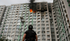 Photo prise et publiée par les services de secours ukrainiens le 1er septembre 2026, montrant un policier devant un immeuble d'habitation en feu à Kiev, après une frappe russe ( Service de secours ukrainiens / Handout )